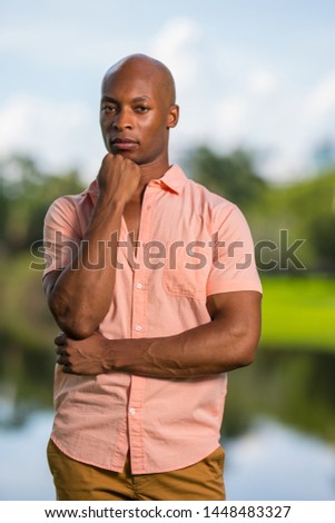 Portrait of happy mature African American man wearing a pink button summer shirt and looking at camera outdoor. Man with hand under chin feeling confident. 
