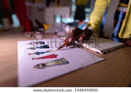 Mid section of African american female fashion designer looking at sketch in design studio. This is a casual creative start-up business office for a diverse team