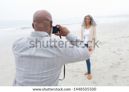 Rear view of African american man taking a picture of mixed-race woman at the beach. Authentic Senior Retired Life Concept