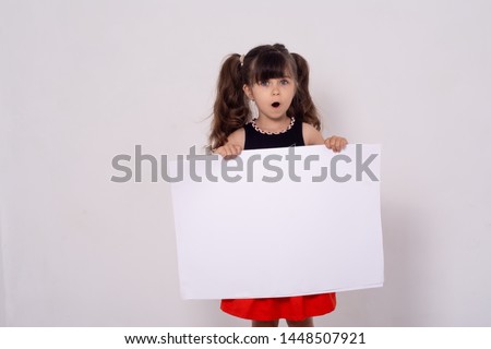 Excited kid with white template. Advertising place for you, empty card, cute kid holding it. Photo of positive schoolkid behind partition looking at camera.