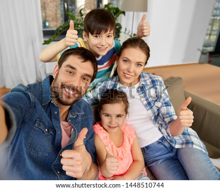 family and people concept - happy father, mother, little son and daughter taking selfie and showing thumbs up at home