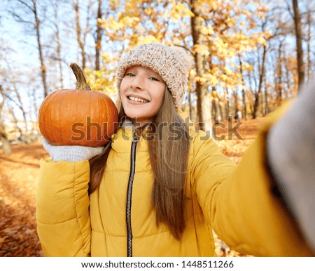 season and people concept - happy girl with pumpkin taking selfie at autumn park
