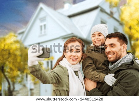family, leisure and people concept - happy mother, father and little daughter taking selfie by smartphone over house in autumn background