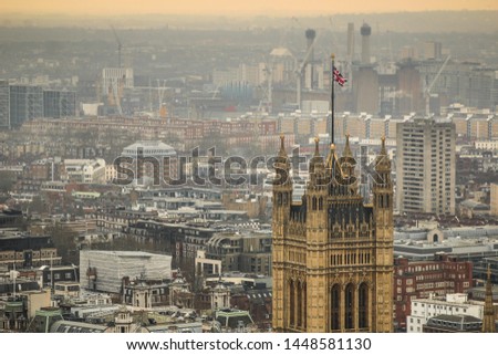 A british flag at the top of Westminster palace, with london in the background.