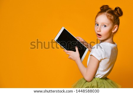 surprised red-haired girl school girl holding a tablet and looks into it. back view. Child playing game, surfing or watching cartoon