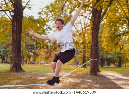 Young man balancing and jumping on slackline. Man walking, jumping and balancing on rope in park. Royalty-Free Stock Photo #1448619509