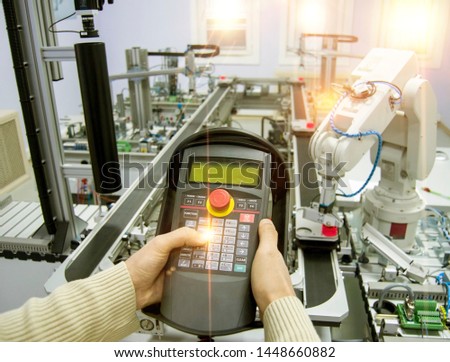 Man is holding teach panel (tablet) to control a robotic arm which is integrated on smart factory production line. industry 4.0 automation line which is equipped with sensors and robotic arm.