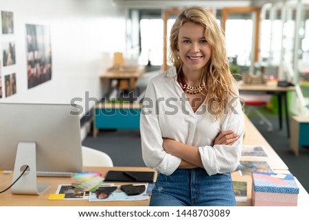 Portrait of Caucasian female graphic designer with arms crossed sitting at desk in a modern office. This is a casual creative start-up business office for a diverse team Royalty-Free Stock Photo #1448703089