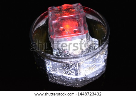 Delicious carbonated drink with red and white ice cubes in a glass of champagne. Glowing ice cubes with LED lighting illuminate the top of the glass and air bubbles in the cocktail.