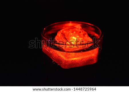 Delicious carbonated drink with red ice cube in a glass of champagne. Glowing ice cube with LED lighting illuminate the top of the glass and air bubbles in the cocktail.