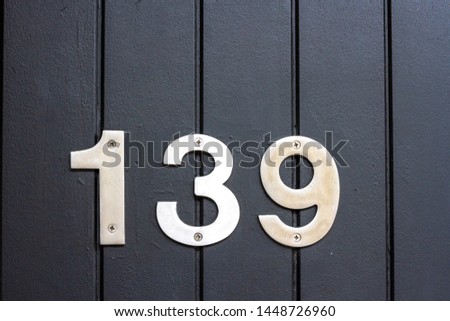 House number 139 with the 139 in silver metal digits on a black wooden front door with planks