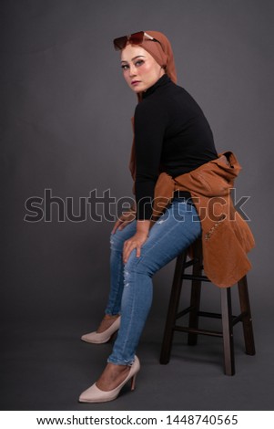 Fashionable young woman in jeans, long sleeves leather jacket and hijab isolated on grey background. Stylish Muslim female hijab fashion lifestyle portraiture concept.
