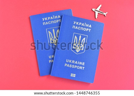 Two Ukrainian id passport with a golden symbol trident on red backdrop and wooden airplane. Biomedical Ukraine id passports on red background with selective focus and empty space for photo or text. 