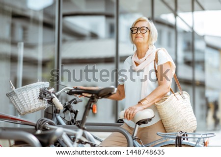 Elegant senior woman parking a bicycle near the modern building outdoors. Concept of an active lifestyle on retirement age
