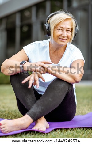 Portrait of a happy senior woman in sports clothes with headphones outdoors. Concept of a healthy lifestyle on retirement