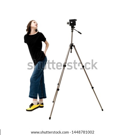 Beautiful brunette girl in a jacket and jeans on a white background posing in front of an old vintage movie camera mounted on a tripod, in isolation