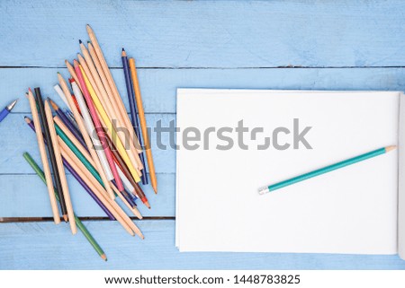 colored pencils and an album with space for text on a blue wooden background. the view from the top