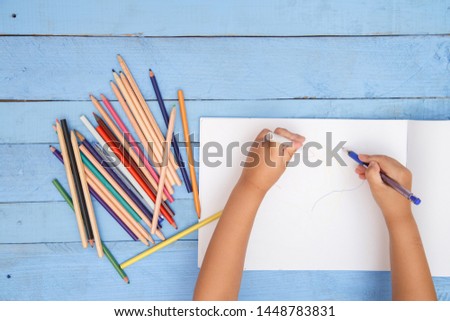 children's hands draw with pencils in the album on the blue table