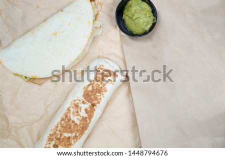 Taco and Burrito with Avocado cream sauce or Guacamole on brown paper or baking paper as background space from fast food restaurant   