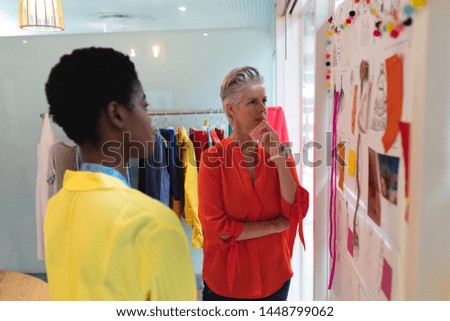 Side view of thoughtful diverse female fashion designers looking over sketch design in design studio. This is a casual creative start-up business office for a diverse team