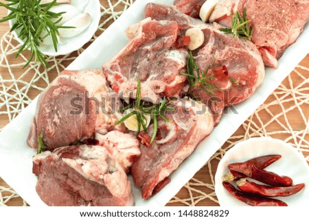 Raw lamb pieces marinated with rosemary, olive oil, garlic and red pepper on a white plate. Close-up. Food photography in high resolution.