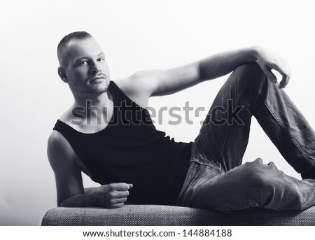 young man lying on a sofa, looking at the camera, muscle shirt and jeans, well maintained and built, black and white portrait