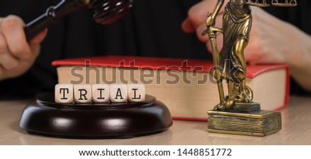 Word TRIAL composed of wooden dices.  Wooden gavel and statue of Themis in the background. Closeup