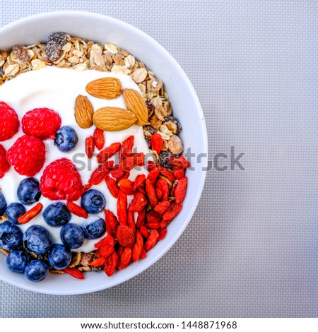 Healthy Vegetarian Breakfast Bowl Of Muesli With Fresh Fruit, Raspberries And Blueberries, Nuts Goji Berries And Yogurt In White Bowls, On A Grey Background