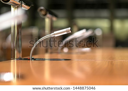 Isolated view of a microphone in the front of a conference room among blurred other mikes in the background - close-up with selective focus and very little depth of field and much copyspace Royalty-Free Stock Photo #1448875046