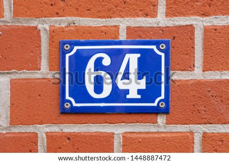 Vintage style house number 64. Metal sign on brick wall.