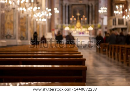 row of old mediterranean wooden benches in a church with blurred background