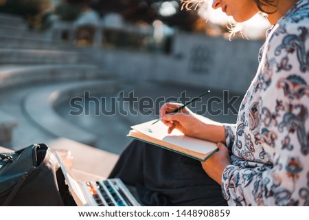 Pretty female artist sitting outdoors painting with watercolors on a sunny afternoon