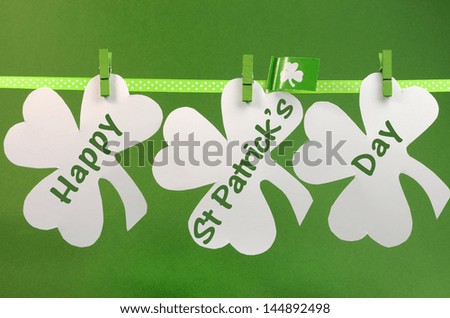 Celebrate St Patrick's Day holiday on March 17 with Happy St Patricks Day message greeting written across white shamrocks hanging from pegs on a line against a green background.