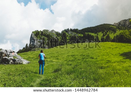 Young woman with backpack takiing pictures in the Ciucas Mountains in Romania on a sunny day of summer