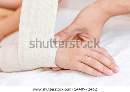 Broken wrist with bandage in hospital office. Doctor is bandaging limb of patient. Sprain, stress fracture, trauma in hand. Child broken arm. Nurse helping customer. First aid. Royalty-Free Stock Photo #1448972462
