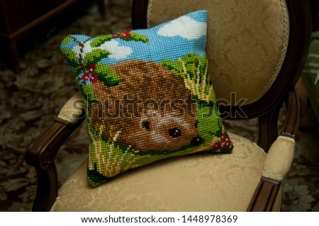 The cross stitched pillow with Hedgehog lies on a chair in retro style. Interior decoration and handicrafts.