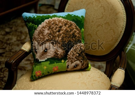 The cross stitched pillow with Hedgehog lies on a chair in retro style. Interior decoration and handicrafts.