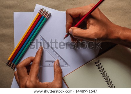 The hands of people who are using pencils and rulers and educational equipment, written on white paper, brown background.
