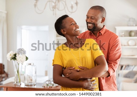 Mature married couple embracing in living room while looking at each other. Newly wed african couple in love hugging at home. Romantic husband with beautiful wife in love at home with copy space. Royalty-Free Stock Photo #1449002381