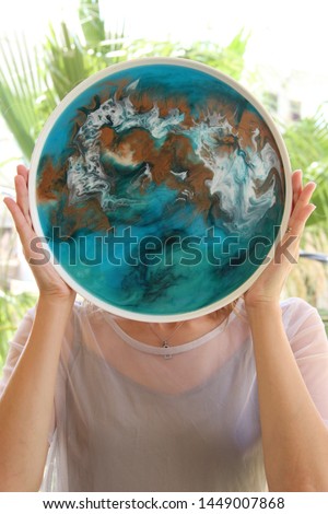 
beautiful girl in a gray dress holding a hand-made tray. The tray is decorated with epoxy resin in blue white and gold color. fluidart, resinart Royalty-Free Stock Photo #1449007868