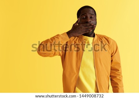 Sleepy tired black man yawning on yellow background portrait. Exhausted african american male model closing mouth with hand felling fatigue, studio shot