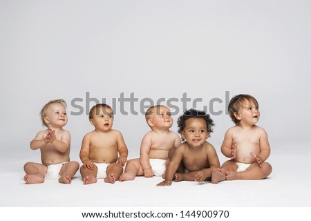 Row of multiethnic babies sitting side by side looking away isolated on gray background Royalty-Free Stock Photo #144900970