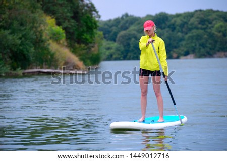 young girl-surfer riding on the stand-up paddle board in the clear waters of the on the background of green trees