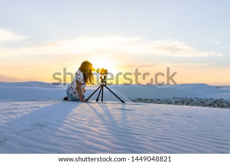 Woman photographer with tripod camera doing time lapse in white sands dunes national monument in New Mexico view of sunset