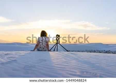 Woman photographer sitting with tripod camera doing time lapse in white sands dunes national monument in New Mexico view of sunset