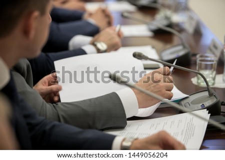 One of politician sitting by table with his hands over document during political summit or conference