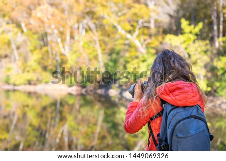 Young woman photographer with backpack and camera taking photo, photographing Great Falls autumn foliage view with river reflection in Maryland
