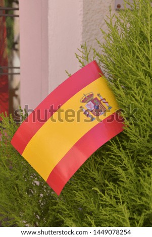 A plastic flag of Spain is stuck in a green bush - concept to the pride of Spain