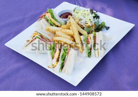 Picture of white plate of club sandwich on the purple table