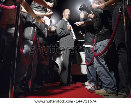 Excited man on red carpet by limousine posing in front of paparazzi
